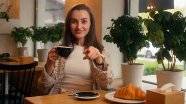 Kafkasyalı kadın kafeteryada oturmuş çay içiyor. Hey sen işaret ediyorsun. Buraya gel ve kameraya bak. Kafeteryada masaya otur ve ayçörekli kahvaltıyı davet et.