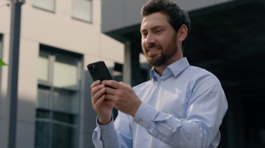 Şehirde cep telefonu kullanan gülümseyen bir iş adamı. Kafkasyalı mutlu erkek işadamı. 40 'lı yaşlarda iş adamı. Elinde akıllı telefon uygulaması olan bir girişimci.