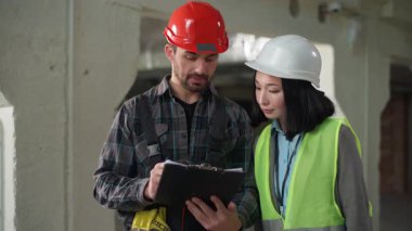 Çok ırklı müteahhitler üniformalı. İnşaat sözleşmesi imzalıyor. Beyaz erkek, kadın, iş kadını imzalı belge yazıyor.