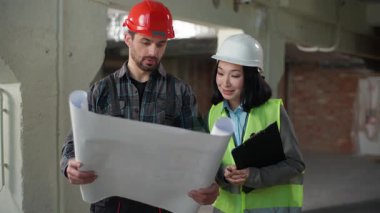 Üniformalı çok ırklı müteahhitler taslak teftişi iş mühendisleri Kafkasyalı erkek Koreli kadın inşaat projesini tartışıyorlar.