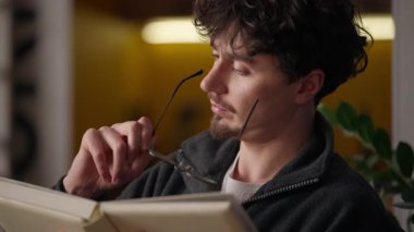 Düşünceli, düşünceli İspanyol adam evde kitap okumayı düşünüyor kafası karışmış hippi okuyucu sayfaları okuyor klasik edebiyat okuyan adam düşünce kütüphanesinde kaybolmuş gözlüklü adam.