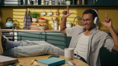 Afro-Amerikalı etnik adam, mutlu erkek öğrenci, kulaklıklı genç kız, evde dans ediyor, mutfakta dans ediyor, kulaklıklarda rahat erkek müziği çalışıyor, ses dansı yapıyor, dans ediyor, ses şarkılarını dinlendiriyor.