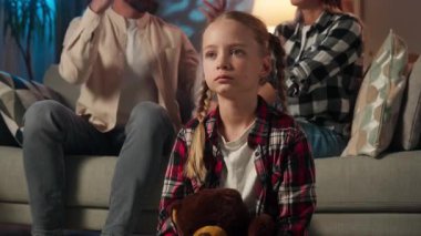 Evde yaşanan aile kavgası sinirleri gerildi. Küçük beyaz kız, elleri kapalı, ailesi koltukta kavga ediyor. Çocuk, çocuk, anne, baba kavgası akşamı.