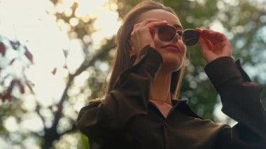 Şık, mutlu, beyaz bir kadın güneş gözlüğü takıyor. Sonbahar şehrinde iş kadını. Etrafa bakıyor, havanın keyfini çıkarıyor.