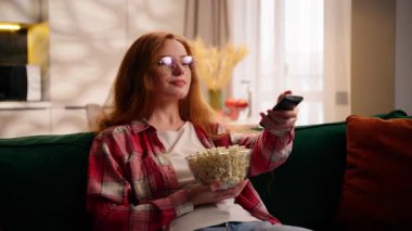 Televizyon kanallarını değiştiren genç beyaz kadın televizyon izlerken hayret içinde, elinde patlamış mısırla evinde dinlenirken kanepede dinlenen film haftasonunu seçiyor.