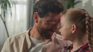 Kafkas aile portresi, kızı ve alınlarına dokunan bir baba, evde baba, sevimli küçük kız çocuk bakımı kavramı ile yakınlık, oturma odasında evlat edinme velayeti sevgisi.