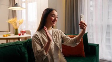 Kafkasyalı kadın cep telefonuyla video konuşmaktan mutlu oluyor. Evde gülümseyen kız sohbet ediyor, akıllı telefon selamlıyor. Merhaba Vlog yayınını oturma odası blogcusu sosyal medyada çevrimiçi kaydediyor.