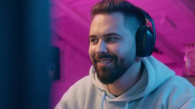 Gülümseyen Kafkasyalı erkek erkek oyuncu flaması bilgisayar oyunu oynamaktan keyif alıyor gamsız, neşeli, bağımlı, online hobi siber spor teknolojisi gece sporlarında kulaklık takıyor.