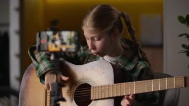 Gitar çalan beyaz tenli küçük kız gitarist çocuk blogcu çocuk blogcu etkileyici internet blogu kameralı tripod müzik enstrümanı.