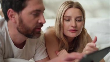 Yatak odasında tablet teknolojisi kullanan mutlu Kafkasyalı çift karı koca, internetten yemek siparişi veren sosyal medya ortakları.