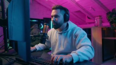 Mutlu beyaz erkek arkadaş bilgisayar akışında zaferi kutluyor kulaklıklar ve mikrofonla neon odasında neşeli oyuncu çevrimiçi savaş reaksiyonunu kazandıktan sonra heyecanlanıyor sevinç reaksiyonu kazananı