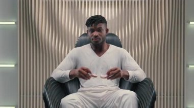 Afrika kökenli Amerikalı erkek, güneş gözlüğü takıyor. Kameraya bakıyor. Fütürist beyaz fütürizm yenilikçiliğinde oturuyor.