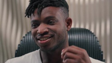 Mutlu gülümseyen Afrikalı Amerikalı adam, etnik erkek, kulaklığa kablosuz kulaklık takıyor, müzik dinliyor, kulaklıkla müzik dinliyor, fütüristik beyaz stüdyo fütürizminde rahatlıyor.