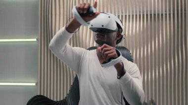 Afro-Amerikalı etnik erkek adam VR oyun yeniliği internet oyunu oynuyor gelecekteki stüdyoda interaktif sanal gerçeklik gözlüğü takıyor fütürizmi tutuyor.