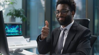 Çevrimiçi iş yerinde çalışan Afrikalı Amerikalı daktilo işçisi. Kameraya bakıp gülümseyen, el hareketi yapan bir işadamı. Onaylayan adam.