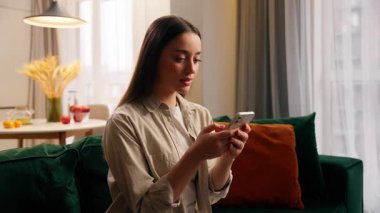 Beyaz kadın evde cep telefonu kullanıyor. Konsantre olmuş kız sohbet ediyor. Akıllı telefon görüşmeleri yapıyor. Oturma odasında yemek siparişi veriyor.