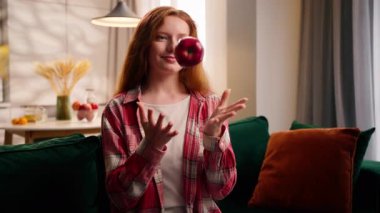 Beyaz bir kadın, gülümseyen bir kadın, elinde taze kırmızı elma koklarken yakalanır. Kapalı alanda mutlu mesut, sağlıklı yemek tercihleri, rahat bir evde oturup meyve vitamini yiyerek mutlu olur.