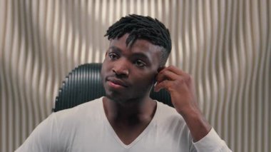 Afrika kökenli Amerikalı erkek, kulaklığa kablosuz kulaklık takıyor, müzik dinliyor, el sallıyor, el sallıyor, kulaklıkla ses şarkısıyla dans ediyor, fütüristik beyaz stüdyonun fütürizminde oturuyor.