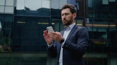 Başarılı bir iş adamı şehirde cep telefonu tutan orta yaşlı bir işadamı. Kafkasyalı erkek işveren, ofis binasının önünde akıllı telefon internet bağlantıları kullanıyor.