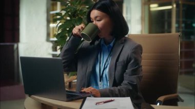 Neşeli, kendinden emin, Asyalı, Çinli iş kadını elinde kupa kahve, gülümseyen iş kadını, kadın yönetici, ofis bilgisayarında bilgisayar bilgisayarında çalışan iş kadını.