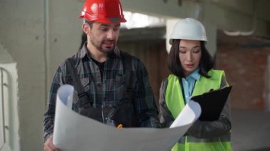 Çok ırklı mimarlar inşaat planı teftişini tartışırken kafatası mühendisi kafası karışmış mühendis işçinin omuzlarını silkmiş Asyalı iş kadını müfettişi stresli bir şekilde konuşuyor.