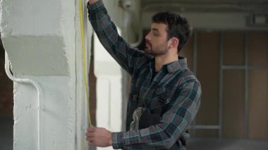 Kafkasyalı mimar duvarları mezurayla ölçer. Alet cetvelini ölçer, tamirci erkek ustabaşı, mühendis inşaat ölçüm aletleri ölçüm hassasiyetini inceler.