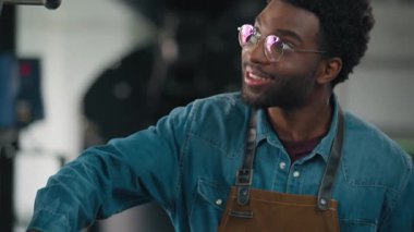 Afrika kökenli Amerikalı bir adam endüstriyel kavrulmuş kahve çekirdeklerini kullanıyor. Önlüklü işçi işçi endüstrisinde çalışıyor. Modern fabrikada ekipman işlemleri konusunda uzman barista.