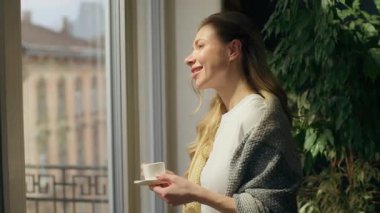 Rahat, mutlu, beyaz kadın kahve içiyor. Pencere bakıyor. Huzur içinde dinleniyor. Ev sahibi kadın çay içiyor.