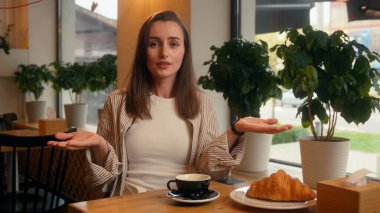 Kafede bekleyen beyaz kadın randevusu iptal edilmiş üzgün yalnız kız kafeterya masasında omuzlarını silkiyor geç saate kadar kamera gecikmesi yüzünden üzgün sabırsız gecikme toplantısı