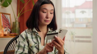 Asyalı Koreli kadın elinde cep telefonu akıllı telefonu tutuyor banka kartı ödemesi kadın kredi kartı teslimat uygulaması alıcısı kapalı mekanda ödeme yapan iş kadını internet üzerinden internet üzerinden ev satın alıyor.