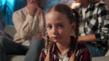 Aile içi şiddet, üzgün küçük beyaz kız, kameraya bakıyor üzgün surat ifadeleri, ebeveynler kanepe üzerinde tartışıyor çocuk, mutsuz anne baba kavgası, evde akşam vakti.