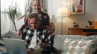 Kafkas aile problemi, çoklu görev yapan anne, kızının gürültülü kötü davranışlarını vurguladı. Kadın, dizüstü bilgisayarda çalışıyor. İki cep telefonu defteri, uzak mesafelere gidiyor.