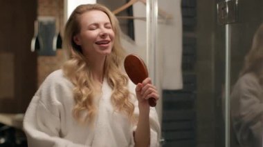 Kafkasyalı mutlu bir kadın model banyodaki kadın bornoz dansında saçlarını tarayıp şarkı söylüyor. Mikrofon şarkıcısı taklidi yapıyor. Komik saç stili.