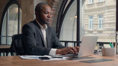 Orta yaşlı Afro-Amerikan girişimci dizüstü bilgisayarları tarıyor, bilgisayar yazıyor internet etnik iş adamı ofis işadamı iş adamı, bilgisayar başında masa işvereni ile çalışıyor.