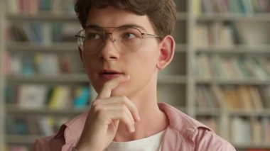 Kafkasyalı erkek öğrenciyi kapatın. Düşünceli düşünen ergen. Düşünceli. Kütüphanede tereddüt eden, kitapları seçen.