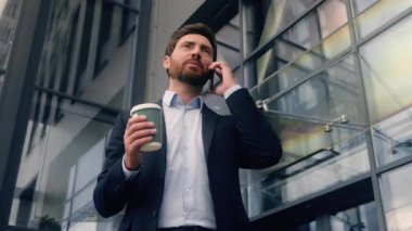 Orta yaşlı Kafkasyalı iş adamı elinde kahve bardağıyla şehirde cep telefonuyla konuşuyor. İş adamı, ofis dışında akıllı telefon ile iletişim kuruyor. Pazarlık yapıyor.