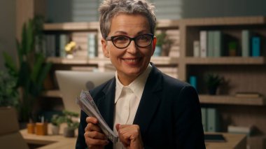 Portre mutlu, komik, beyaz, iş kadını yaşlı, yaşlı, olgun, emekli kadın işkadını para kokusu alan, para kokusu alan, finans paraları koklayan, kameraya bakan.