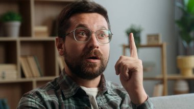 Düşünceli, düşünceli, tereddütlü, kararsız, düşünceli, kafası karışmış, kafası karışmış, kafatası karışık bir erkek evin içinde kameraya gülümseyen yaratıcı çözümler bulmaya çalışıyor.