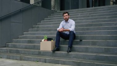 Stresli Kafkasyalı orta yaşlı iş adamı işinden kovuldu ofis binasının yanındaki merdivenlerde oturan işadamı üzgün düşünen işadamı finansal krizin sona erdiğini düşünüyor.