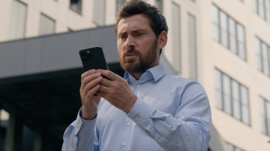 Kızgın, orta yaşlı, olgun iş adamı, şehir merkezinde akıllı telefon kullanmaktan rahatsız olan iş adamı, kızgın işveren, cep telefonu, spam mesajı, dışarıda çalışmaktan rahatsız oluyor.