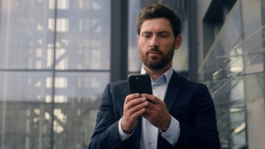 İşadamı erkek işadamı cep telefonu kullanıyor. Şehir işvereni yetişkin girişimci dışarıda yürüyor. Ofis çalışanlarının yanında yürüyor.