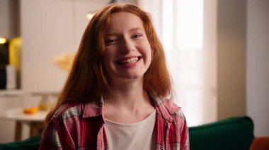 Sağlıklı beyaz dişleriyle evde gülümseyen mutlu bir kadın dişlek beyaz kız tatmin olmuş gülüyor. Oturma odasında kameraya bakıyor. Neşeli, kaygısız bir kadın.