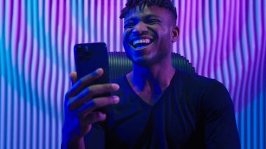 Afrikalı Amerikalı erkek kapalı mekanda yenilikçi siber uzay ışıkları cep telefonuyla kazanıyor online bahis kumarhanesi zafer kazanmak için mutlu video oyunu bağımlısı çığlıklarını kutluyor