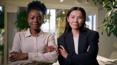 İki kendine güvenen iş kadını çok ırklı Afrikalı kızlar ofiste yan yana poz veren Çinli Amerikalı iş ortakları profesyonel iş arkadaşları iş arkadaşları.