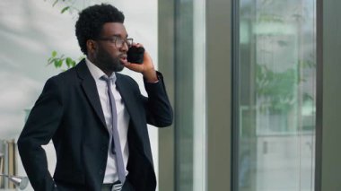 Kızgın kızgın kızgın kızgın Afrikalı Amerikalı iş adamı konuşuyor cep telefonu sorununu tartışırken ofiste öfkeli iş adamı erkek işadamı işvereni pencereye bakarak tartışma kavgası ediyor