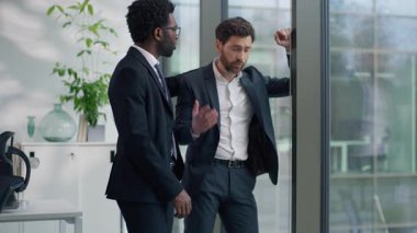 İki çok ırklı iş adamı ofiste Kafkasyalı üzgün iş adamı pencere kenarında afro-amerikan erkek ortak yatıştırıcı iş adamlarını destekliyor iş sorunları tartışıyorlar