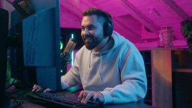 Heyecanlı şampiyon beyaz tenli erkek oyuncu flamalı adam şans kazandı zafer kazandı internet kazandı konuşan mikrofon oyun bağımlısı kulaklıklarıyla karanlık odada oyun oynuyor