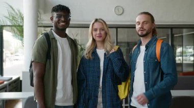 Çok ırklı üç arkadaş çeşitliliği öğrencisinin gülümsemesi başarılı olmayı tavsiye ediyor. Üniversite koridorundaki kameraya birlikte bakıp olumlu işaret işareti yapın.