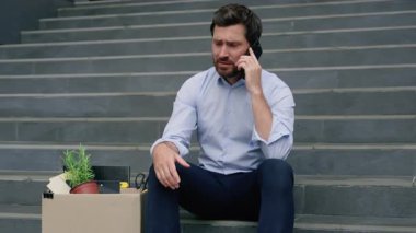 İşsiz, beyaz, orta yaşlı bir işadamı işten çıkarıldı. İşten çıkarma kutusuyla cep telefonundan konuşuyordu. Merdivenlerde ofis binasının yanında oturuyordu.