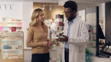 Eczacı doktor, eczane sağlık ürünlerindeki vitaminlerin satın alınmasına yardımcı olur. Afrikalı Amerikalı erkek, beyaz kadın eczane tıbbi konsültasyonu satın alır.